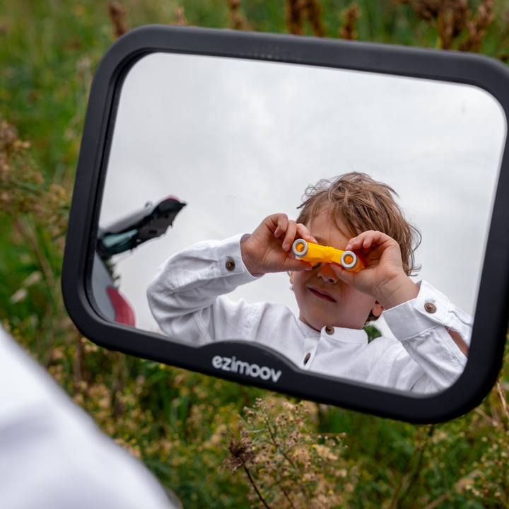 This image shows a child playing with his reflection in the mirror outside the car.