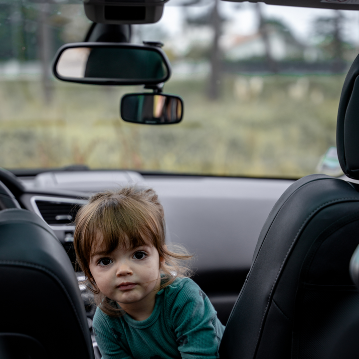 This image shows the Ezimoov Clip-On Rear View Mirror in use in a car, with a child looking at the camera.