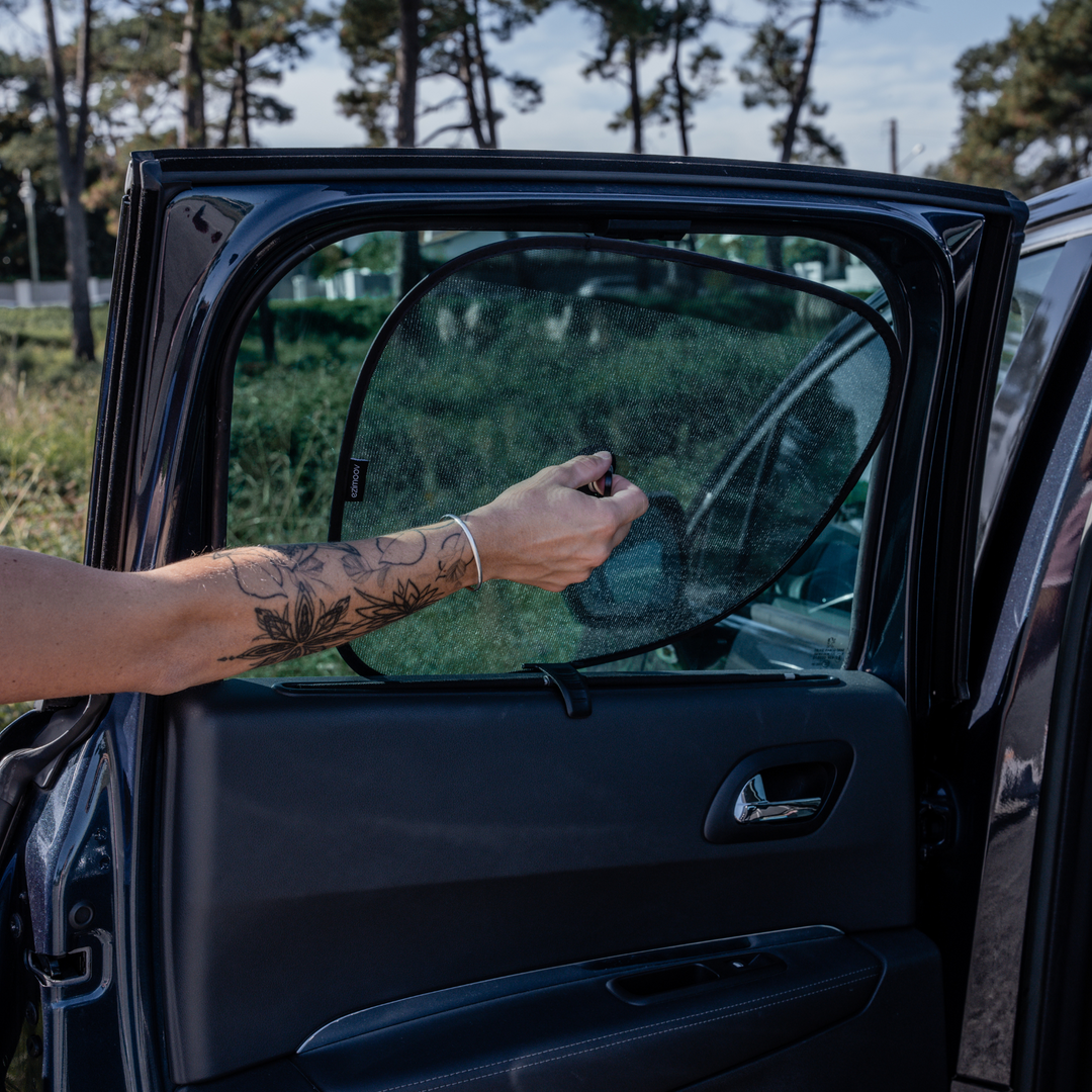 This image shows the Ezimoov sun stopper being installed by a parent on the back of a car window with one hand.