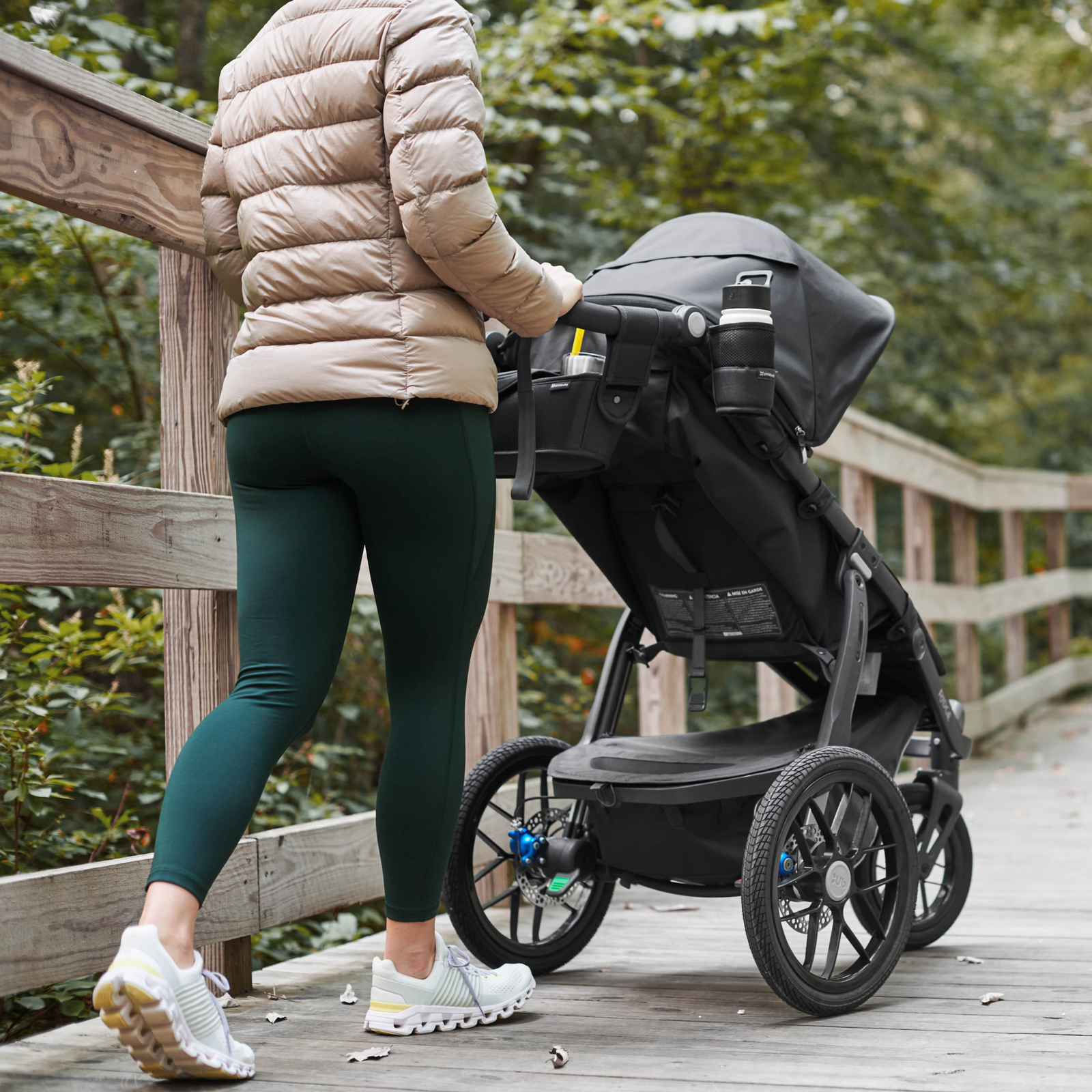 This image is a Mom out for a walk in a forest park with her Ridge stroller, and the collapsible cup holder is holding her water bottle.