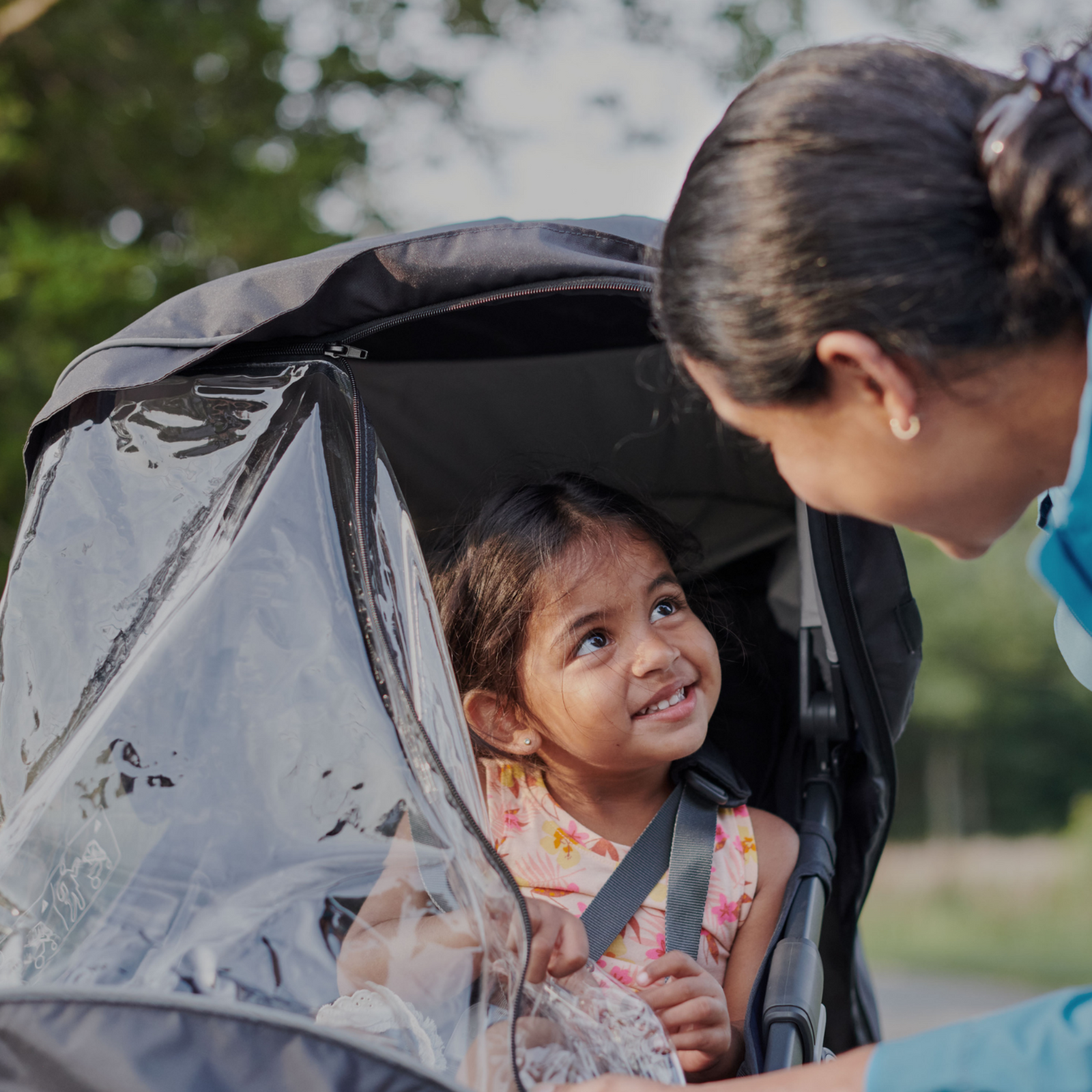 This is a lifestyle image of a Mum out for a walk with her child in the Ridge stroller and she has unzipped the rain cover to check on her child