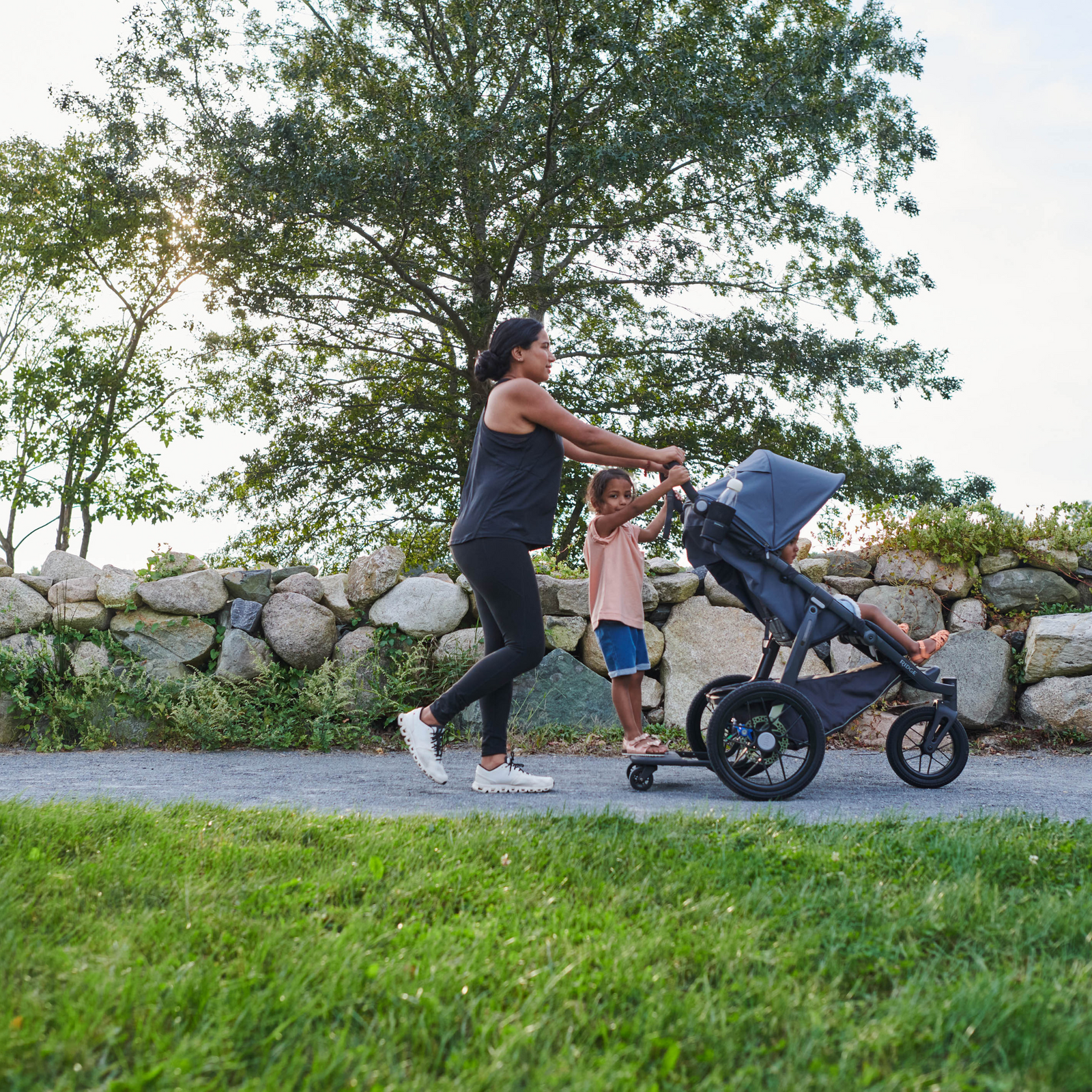 This is a lifestyle shot of a Mum out for a walk with her two kids. One child is in the toddler seat of the stroller and another is on the piggyback board.