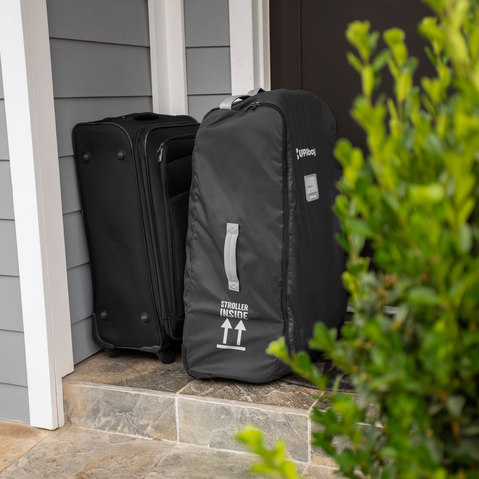 This is an image of the UPPAbaby Travel Bag beside a suitcase at a front door, ready to be loaded into the car